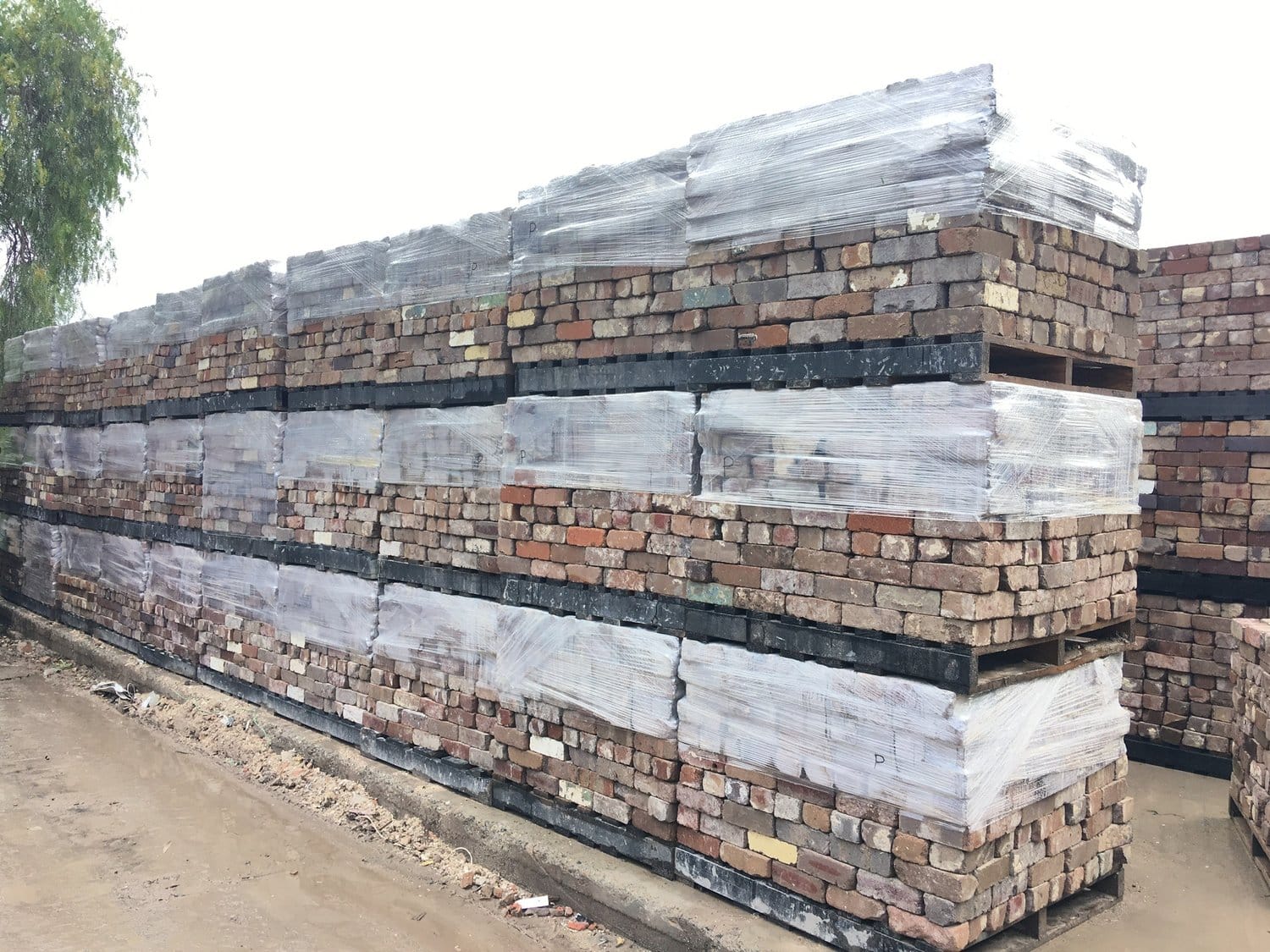 Stacks of premium reclaimed bricks wrapped in plastic sheeting, arranged in neat rows on a concrete surface.