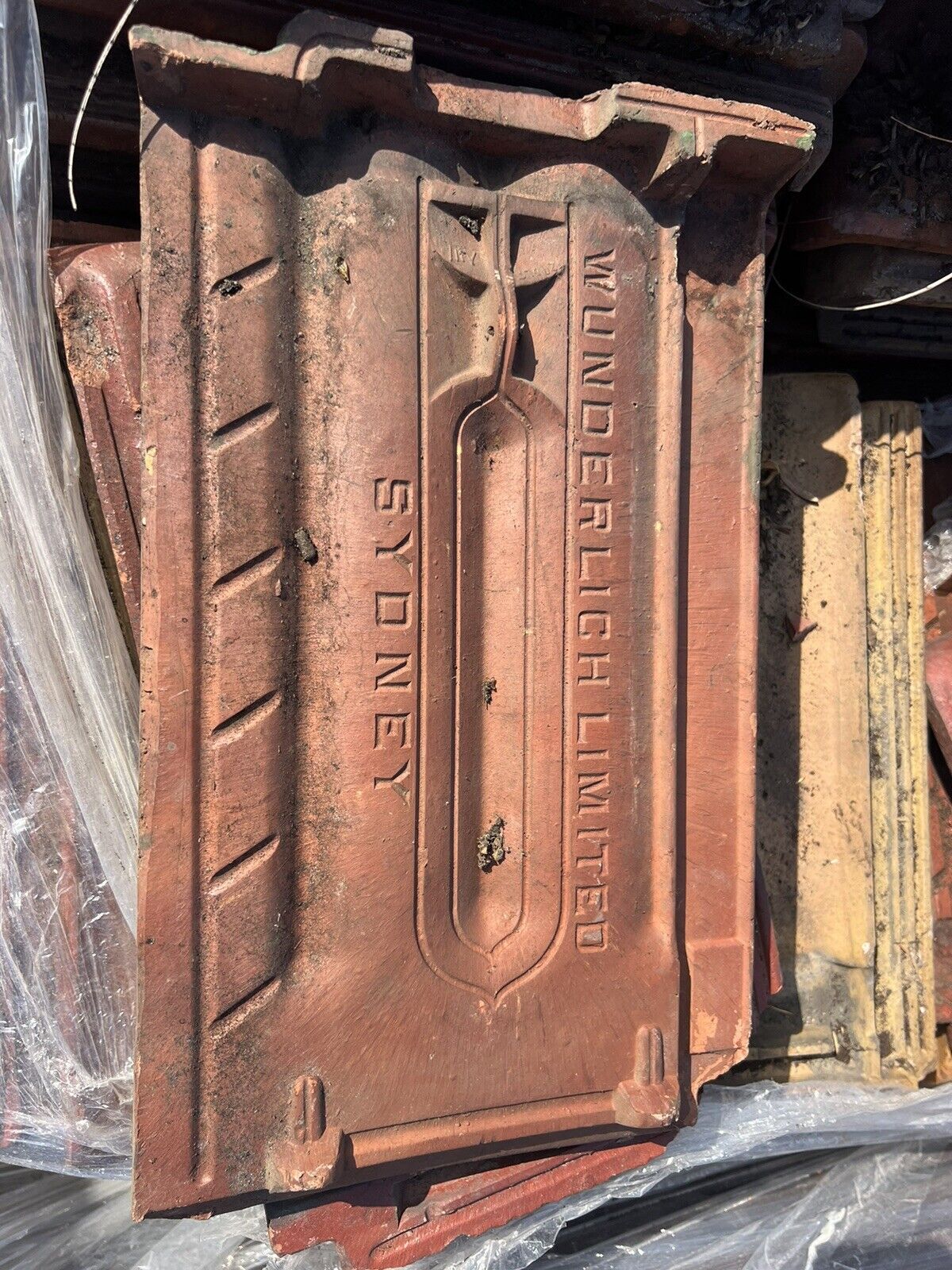 Wunderlich Limited terracotta roof tile from Sydney, showing embossed lettering and design details, placed on a stack of similar tiles.