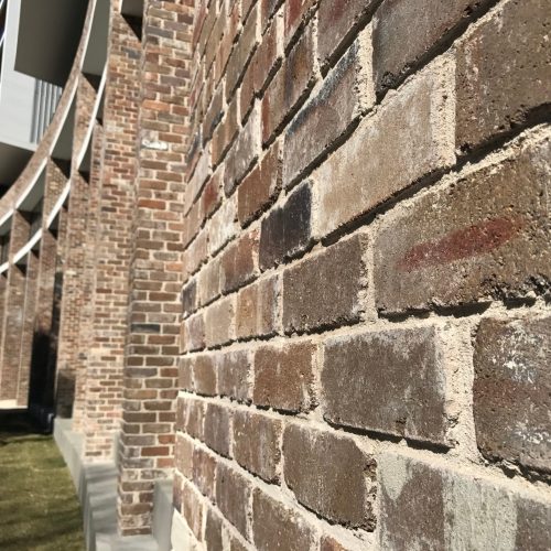 Close-up of a brick wall with the elegant curve of Parc Mezzo's architecture in the background on a sunny day.