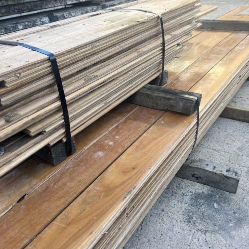 Stacks of premium reclaimed wooden planks, secured with black straps on a concrete surface.