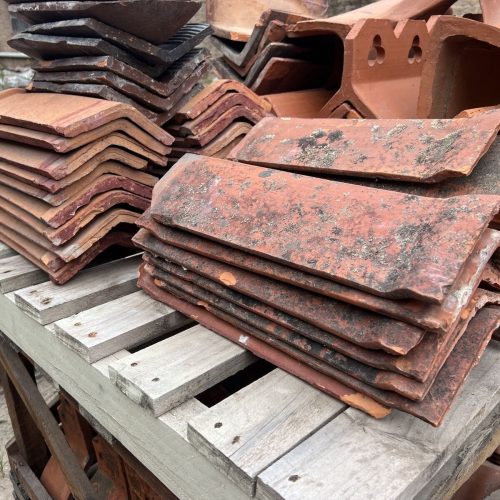 Stacks of premium reclaimed building materials, including weathered red roof tiles, rest neatly on a wooden pallet.